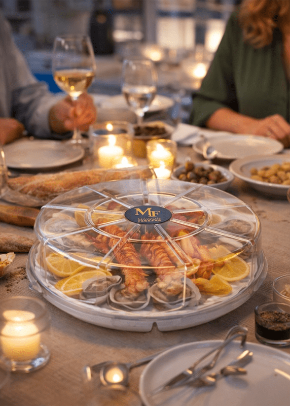 Plateau pour fruits de mer avec couvercle transparent Ecopack Concept posé au centre d’une table lors d’un repas convivial.